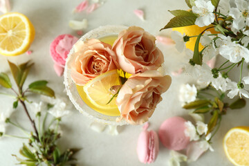 Glass of cocktail, ingredients and flowers on white textured table