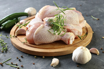 Raw chicken legs with spices on a board on a black background.