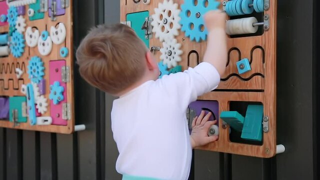 The Kid At The Busy board. Cute boy playing with a busy board on the wall. Educational toys. Busy-board for children. Wooden game board. Selective focus