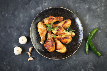 Fried chicken legs with spices in a plate on a black background top view.