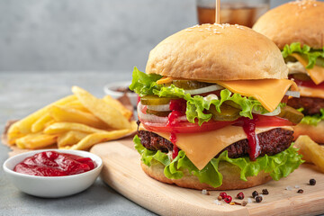 Large burger with beef patty, cheese, sauce, vegetables and salad on a gray background. Side view, close-up.
