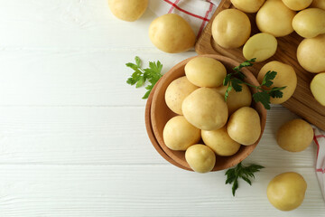 Wooden bowl with young potato on white wooden table