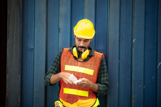 employee foreman men worker smoking cigarette tobacco nicotine whlie take a break, relax work lifestyle concept, container site, outdoor smoking, men wearing safety vest, helmet and headphone
