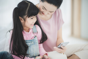 mother and daughter happy family time concept at home, using telephone and headphone, dancing girl, mom and child, parent, living room at home on the sofa, white background, happy girl wearing pink