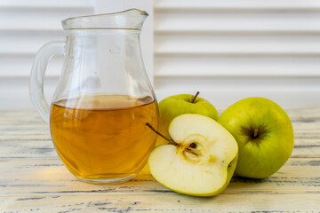 Green apples and jug with apple juice on wooden background