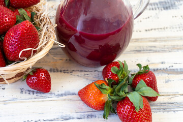 Strawberry in basket and on table on wooden background, strawberry juice in jug