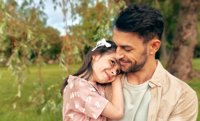 Portrait of a smiling father embracing his little daughter in the park.