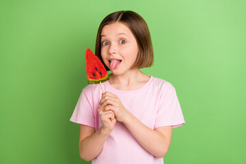 Photo of young little girl happy positive smile lick eat lollypop dessert sugar tasty isolated over green color background - obrazy, fototapety, plakaty