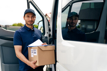 Portrait of courier holding cardboard box and documents