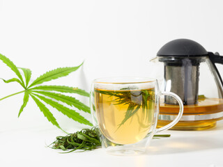 Cannabis tea cup with  marijuana fresh green leaves and flower  in glass cup, CBD oil brown bottle and kettle  on white background.