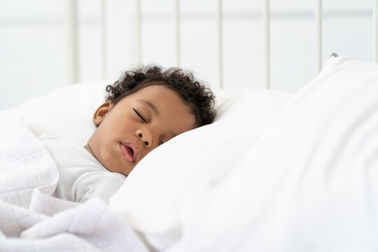 black african american baby sleeping on a white mattress.