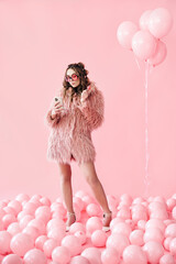 Full length portrait of glamour young woman typing on mobile smartphone over pink balloons background
