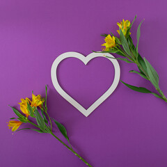 two fresh yellow flowers with green leaves and heartshape frame on purple bold background with copy space. minimal decorative luxury background art. minimal flat lay.