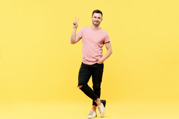 Fototapeta na wymiar Full length portrait of trendy handsome man show victory sign on yellow background