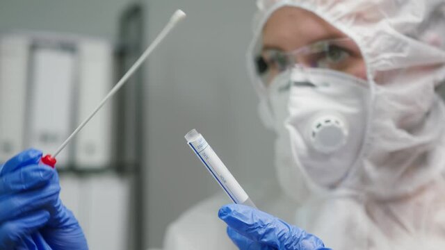 PCR test in laboratory, doctor holding COVID-19 Coronavirus swab collection kit, wearing PPE protective suit mask gloves, test tube for taking OP NP patient specimen sample, writing the results
