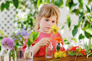Obraz na płótnie Canvas Little preschool girl making flower bouquet at home. Toddler child putting colorful garden summer flowers in small bottles with water. Home activities for kids. Flowers in rainbow colors. Happy child.