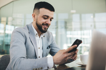 Positive businessman using smartphone in creative workplace