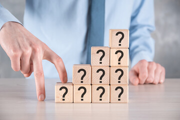 Businessman hold and put wooden cube block shape with question marks on grey table. Space for text.concept for confusion, question or solution