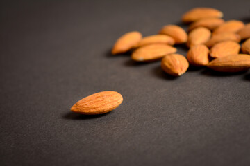 Close-up to Almond nut on dark background. One nut in focus. Scattered almonds. Creative food concept. Raw nuts. Copy space image. Single object. Kitchen still life
