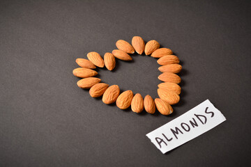 Side view of heart shape of almond nut near piece of paper with hand drawn text almonds on dark background. Food heart silhouette isolated. Single object. Copy space image. Creative concept
