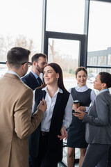 Fototapeta premium Smiling businesswoman standing near colleague and multiethnic business people in office