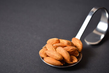 Side view of Almond nuts served on silver metal stainless steel spoon. almonds on dark background. Creative food concept. Raw nuts. Copy space image. Single object. Kitchen still life
