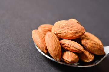 Macro shot of Almond nuts served on silver metal stainless steel spoon. almonds on dark background....