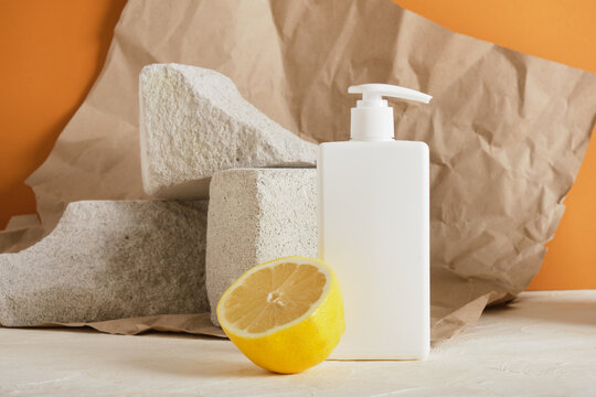 white plastic bottle with a dispenser for soap ioi cream, lemon and concrete podiums, brown background, crumpled paper, mock up cosmetics copy space blank bottle