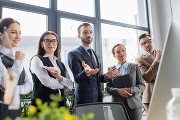 Obraz premium Businessman pointing at computer near interracial colleagues