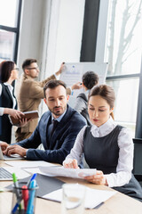 Businesswoman working with paper near colleague and laptops on table