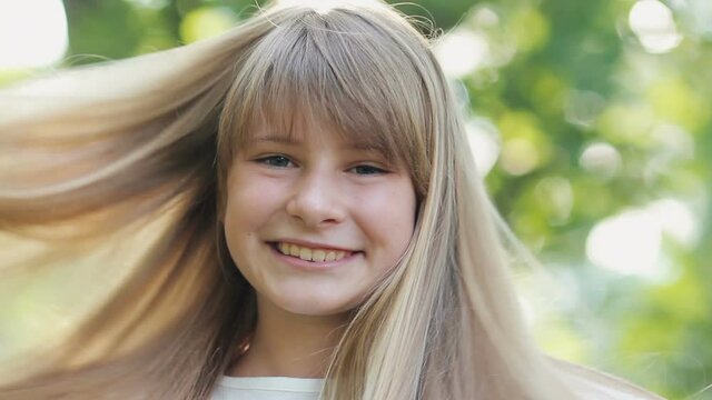 Cheerful teen girl having fun with her long blonde hair in sunlight outdoor