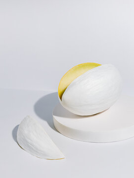 Mellon painted in white with a cut slice isolated on a white background. Honeydew melon vegetable placed on a monochrome matching podium. Creative health food concept.