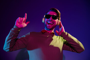 Photo of young cool dj guy wear headphones spectacles sweater isolated on dark blue color background