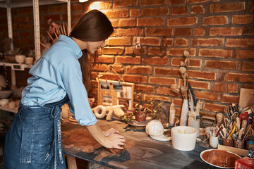 Brunette Caucasian female artisan working with fresh wet earthenware product in art studio