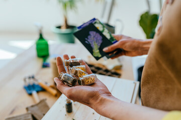 View from above of female gardener holding different seeds for growing in small bottles and seeds...