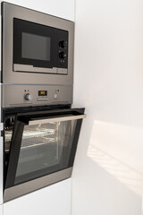 Modern steel microwave and opened oven in kitchen