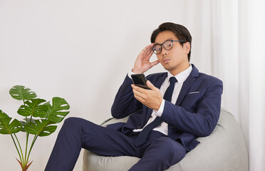 Asian Financial Advisor Wear Glasses Headache from Thinking on Bean Bag in Home Office. Businessman Work at Home for Social Distance or Home Quarantine in Covid 19 or Coronavirus Situation