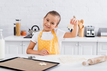 Happy girl holding dough near baking sheet and cookie cutter