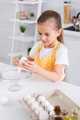 Obraz na płótnie Canvas Kid in apron holding spoon and egg near sugar and oil
