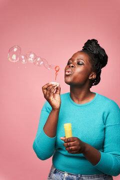 Joyful black woman blowing soap bubbles in studio