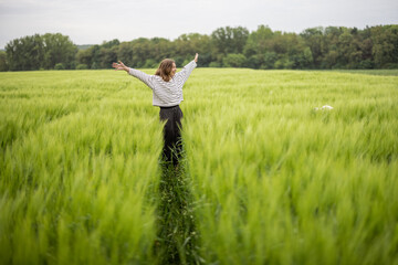 Happy woman with raised hands walking in green rye field and enjoys calm nature. Freedom and...