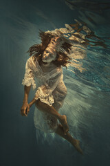 A girl in a white lace dress swims underwater as if flying in zero gravity