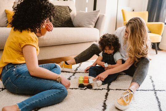 Cheerful lesbian couple playing with child on floor
