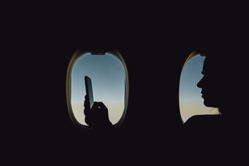 Transport, tourism and technology concept - close up of woman with smartphone traveling by plane and working over porthole background.