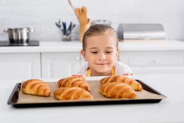 Happy kid looking at blurred croissants on baking sheet