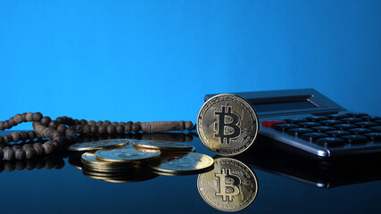 Bitcoins, calculator and tasbih or rosary beads on blur blue background. Conceptual of Islamic Bitcoins Investment.