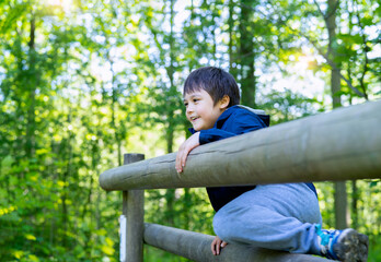 Cute boy with smiling face looking out, Candid shot happy kid playing in the park,Child having fun in a climbing on wooden fame  at adventure park on sunny day summer, outdoor activity, back to school