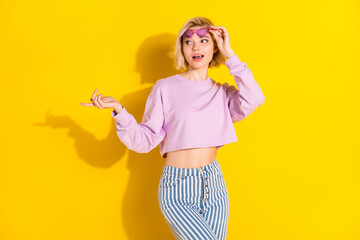 Photo of young girl happy positive smile hand touch sunglass point finger empty space isolated over yellow color background