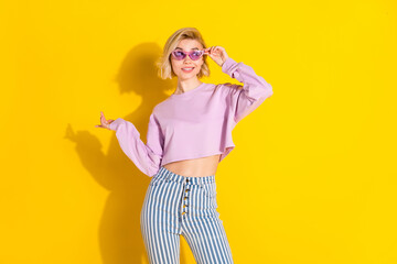 Photo of young girl happy positive smile hand touch sunglass look empty space isolated over yellow color background