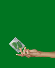Womans hands holding eye patches on green backgound. Face care beauty treatment steps concept
